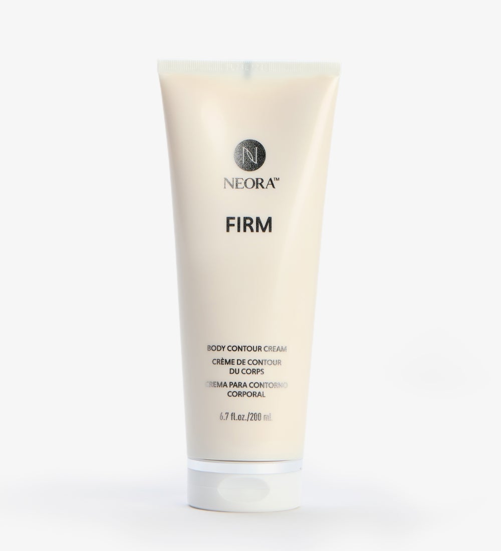 A woman sitting down holding a Firm Body Contour Cream tube in front of her legs.